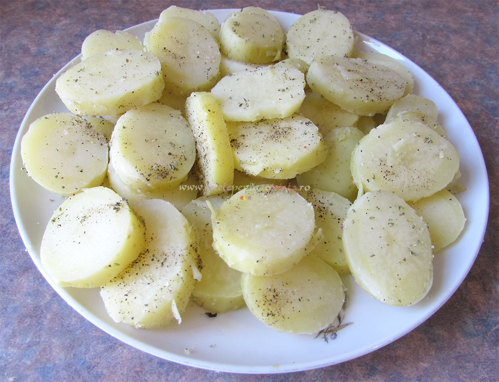Fierbem cartofii intregi timp de aproximativ 10 minute. Ii curatam de coaja si-i taiem rondele. Ii condimentam cu sare, piper si oregano.